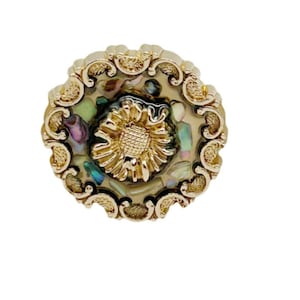 May include: A gold ring featuring a decorative floral design. The centre of the ring is filled with iridescent abalone shell pieces.
