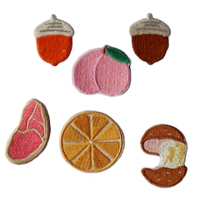May include: A collection of embroidered patches with food and nature motifs. The patches depict an orange acorn, a peach with a green leaf, a brown acorn, a steak, a sliced orange, and a bitten sandwich. Detailed stitching.