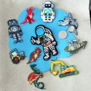 May include: A blue felt patch with various iron-on patches, including a robot, astronaut, dinosaur, helicopter, tractor, excavator, seahorse, and a spaceship.