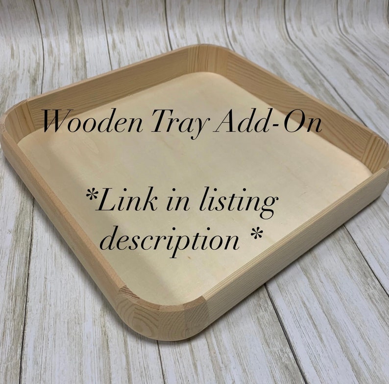 May include: A square wooden tray with rounded corners and a light wood finish. The tray has a recessed interior and the text "Wooden Tray Add-On" and "*Link in listing description*" is printed on the tray.