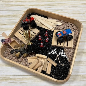 May include: A wooden tray filled with pinto beans and black beans, featuring toy monster trucks, wooden blocks, a gold trophy, miniature traffic cones, and checkered flags. A small wooden scoop with an American flag is also included.