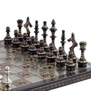 May include: A square chess set featuring a board with alternating black and silver patterned squares. One side has polished silver-toned chess pieces, while the other side has black chess pieces with gold-toned accents. The board edge is black.