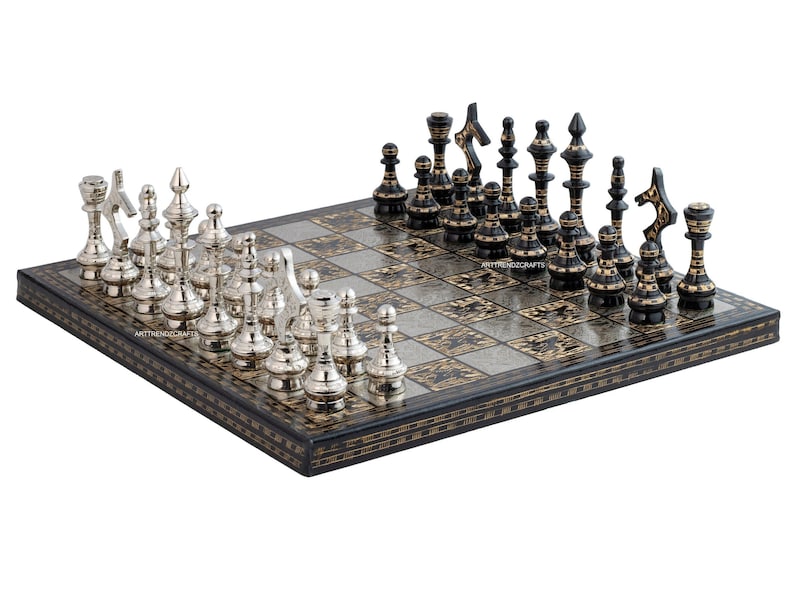May include: A square chess set featuring a board with alternating black and silver patterned squares. One side has polished silver-toned chess pieces, while the other side has black chess pieces with gold-toned accents. The board edge is black.