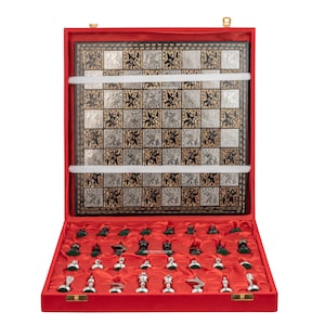 May include: A chess set in a red velvet-lined case featuring a square board with alternating silver and black squares decorated with intricate etched animal figures. The set includes a collection of silver and dark green chess pieces.