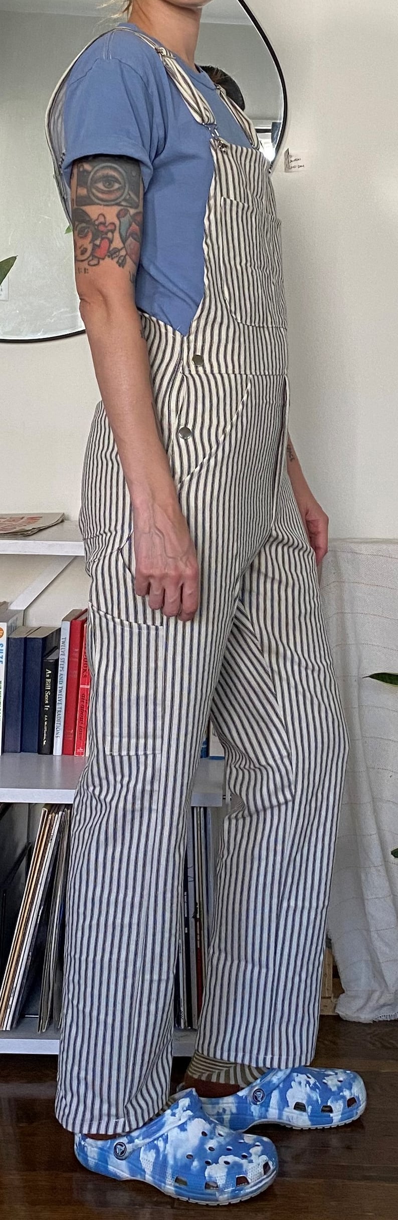 May include: A person wearing blue striped overalls with a light blue t-shirt and blue and white cloud-patterned clogs.