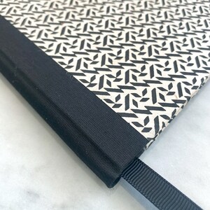 May include: Close-up of a black and white patterned notebook with a black fabric cover and a black ribbon bookmark.