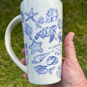 May include: White ceramic mug with a blue and white design of sea life, including starfish, seashells, and a turtle.