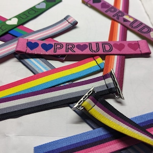 May include: A collection of colourful Apple Watch bands with the word "PRUD" printed on them. The bands feature different pride flag colours and designs.