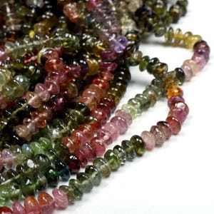 May include: A strand of multi-colored gemstone beads. The beads are faceted and have a smooth, polished finish. The colors of the beads include green, pink, red, and brown.