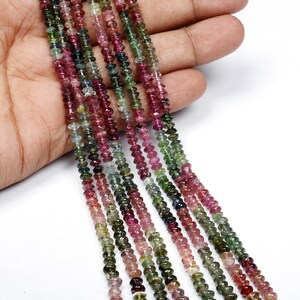 May include: Multicolored Tourmaline gemstone beads, approximately 4mm in size, strung on a strand. The beads are a mix of pink, green, and blue.
