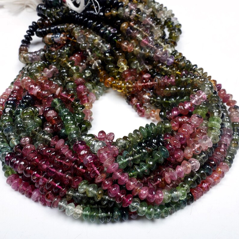 May include: A strand of multi-colored tourmaline beads. The beads are faceted and have a variety of colors, including green, pink, and black. The beads are strung on a clear thread.