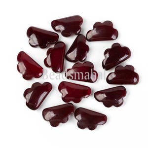 May include: A collection of 14 dark red glass beads shaped like clouds. The beads are glossy and have a slightly irregular shape.