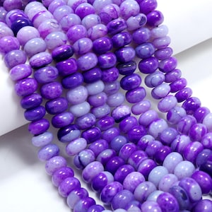 May include: A collection of round, smooth, purple beads arranged in multiple vertical strands. The beads exhibit varying shades of violet and lavender with natural marbled patterns and a polished, glossy finish, creating a uniform texture.