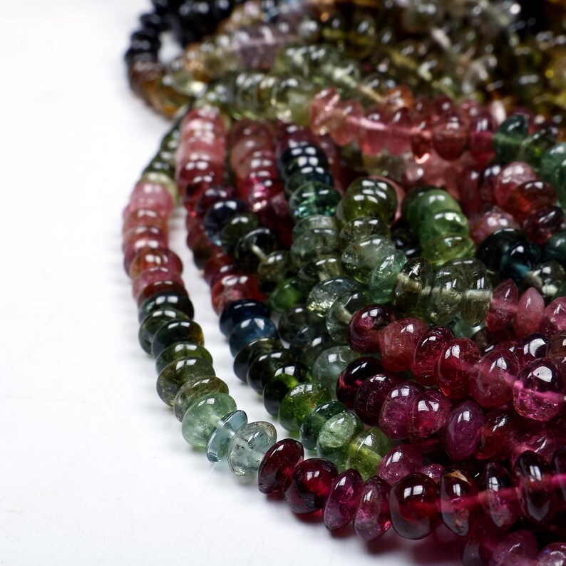 May include: A strand of multi-colored gemstone beads. The beads are round and have a smooth, polished finish. The colors of the beads include pink, green, blue, and black.