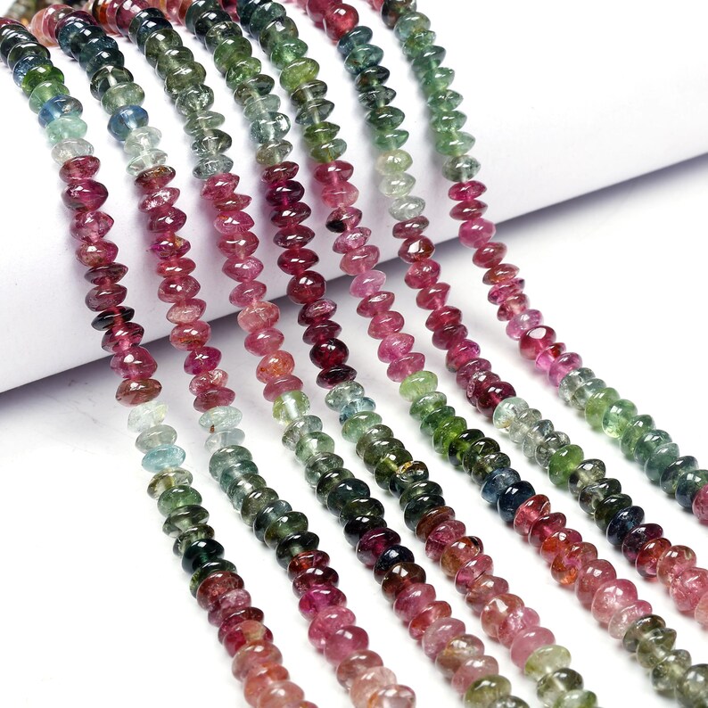 May include: Multicolored gemstone beads in shades of pink, green, and blue. The beads are faceted and have a slightly elongated shape. The beads are strung on a thread and are ready to be used for jewelry making.