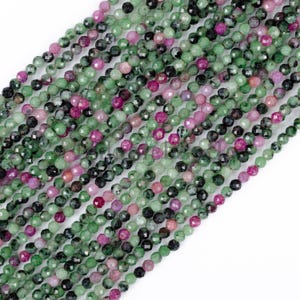Può includere: Primo piano di fili di perline di pietre preziose sfaccettate nei toni del verde, rosa e nero. Le perline sono piccole e rotonde, con una superficie lucida. Le perline sono infilate insieme, creando un aspetto fluido e strutturato. Ideale per la creazione di gioielli.