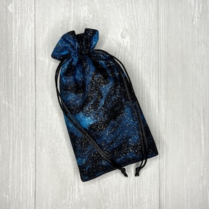 May include: A small blue and black drawstring bag with a galaxy print. The bag has black drawstrings and is made of a soft fabric.