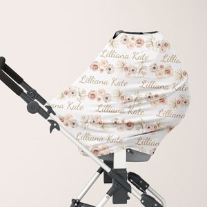 Può includere: Un passeggino bianco con una copertura per passeggino con motivo floreale. La copertura riporta il nome "Lilliana Kate" ripetuto.