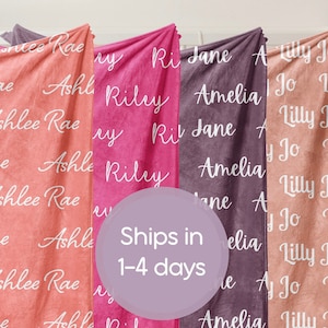 May include: Four personalized fleece blankets with different names printed on them. The blankets are in shades of pink, peach, and purple. The text on the blankets reads: Ashlee Rae, Riley, Jane, Amelia, Lilly Jo.