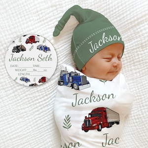 May include: A white swaddle blanket with a green leaf and red, blue, and black semi-trucks printed on it. A baby is swaddled in the blanket. A green knit hat with the name "Jackson" embroidered on it is on the baby's head. A white round tag with the name "Jackson Seth" and spaces for date, weight, and length is in the background.