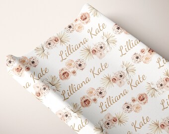 May include: White changing pad cover with a repeating pattern of blush pink and brown floral bouquets and palm leaves. The names "Lilliana" and "Kate" are repeated throughout the pattern.