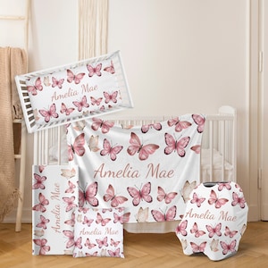 May include: A nursery bedding set with a pink and white butterfly pattern. The set includes a crib sheet, a blanket, a pillow, a burp cloth, and a car seat canopy. The name "Amelia Mae" is printed on each piece.