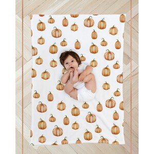 May include: A white baby blanket with a pumpkin pattern. The blanket is made of soft, breathable fabric and is perfect for keeping your little one warm and cozy. The blanket features a cute baby lying on top of it.