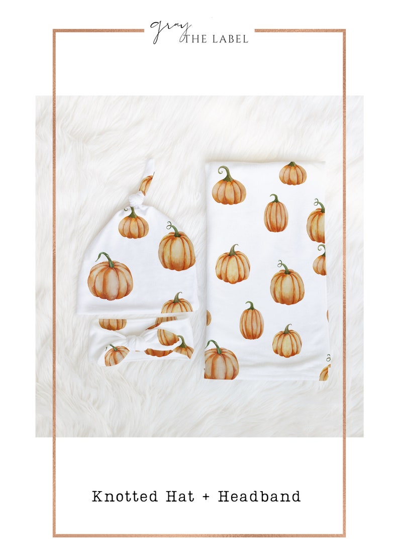 May include: A set of two baby items featuring a pumpkin print. The set includes a knotted hat and a headband. Both items are white with orange pumpkins.