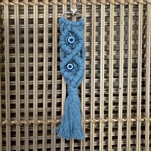 Puede incluir: Un llavero de macram&eacute; azul y blanco con tres amuletos de ojo turco y un borla.