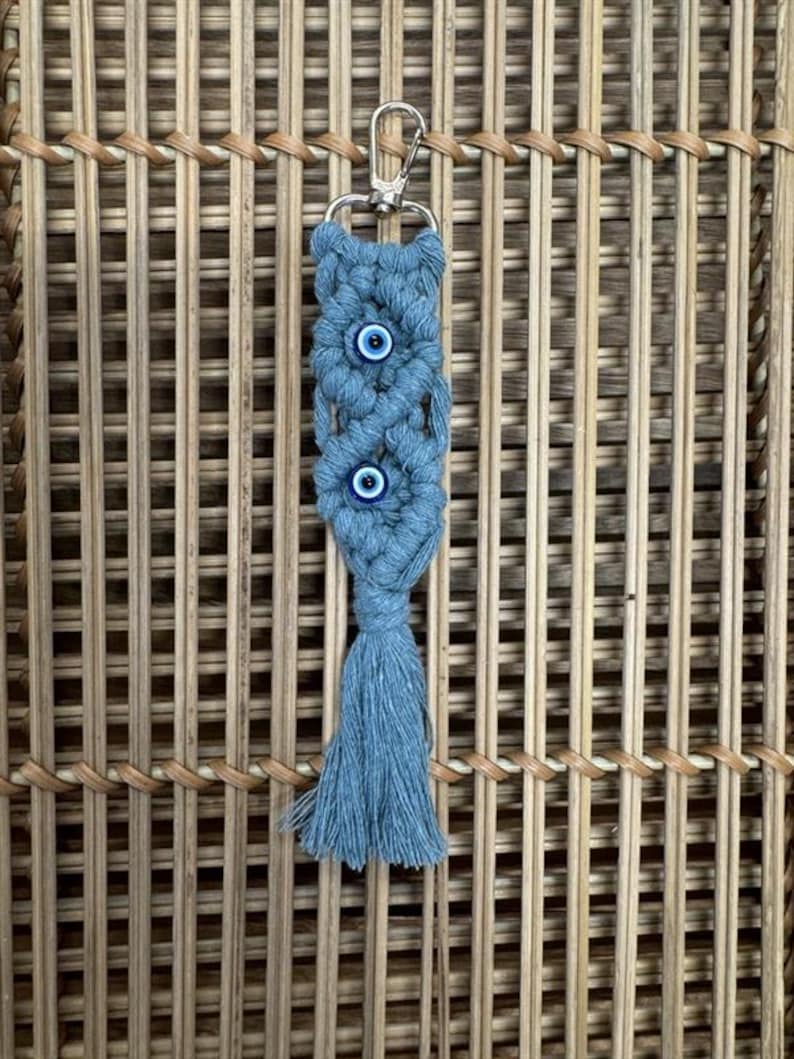 Puede incluir: Un llavero de macram&eacute; azul y blanco con tres amuletos de ojo turco y un borla.