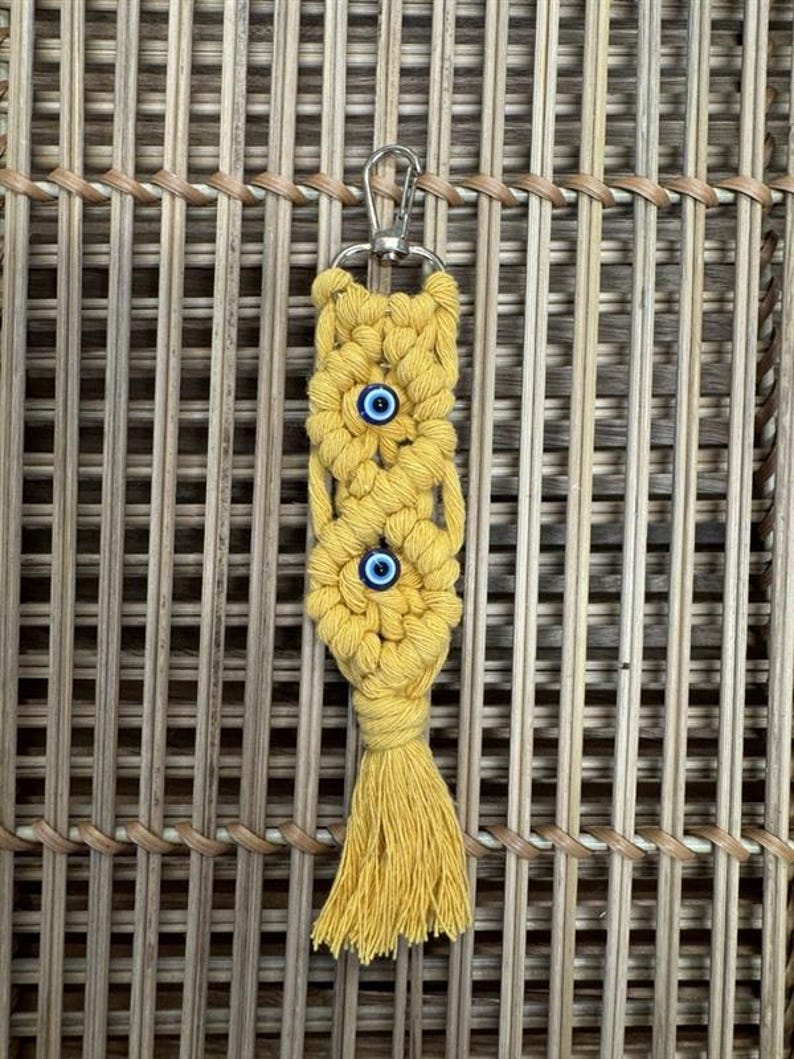 Puede incluir: Un llavero de macram&eacute; amarillo con tres dijes de ojo azul y una borla.