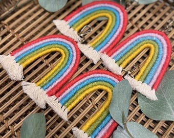 Puede incluir: Cuatro llaveros en forma de arcoíris con un diseño de macramé. Cada llavero presenta una vibrante gama de colores, incluyendo rojo, naranja, amarillo, verde, azul y morado. Los llaveros tienen una franja blanca en la parte inferior y un cierre dorado.