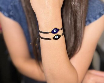 May include: Two black string bracelets with gold evil eye charms. One charm has a blue eye and the other has a black eye.