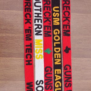 May include: Five beaded lanyards with text in close-up. The lanyards are red, white, and black, with text in black, yellow, and green. The text includes "WRECK 'EM TECH", "SOUTHERN MISS", "USM GOLDEN EAGLES", and "GUNS UP".