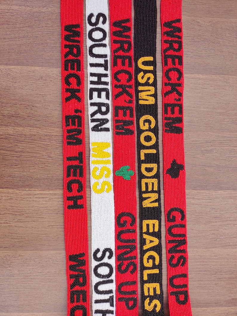 May include: Five beaded lanyards with text in close-up. The lanyards are red, white, and black, with text in black, yellow, and green. The text includes "WRECK 'EM TECH", "SOUTHERN MISS", "USM GOLDEN EAGLES", and "GUNS UP".