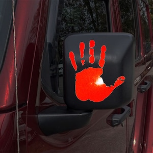 May include: A red handprint decal on a black side view mirror of a red Jeep Wrangler.