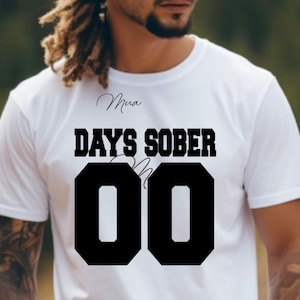May include: White t-shirt with black text that reads "Days Sober" and the number "00" in a large font.