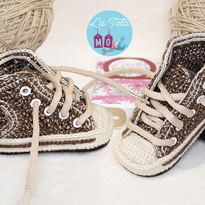 May include: A pair of brown and beige crocheted baby shoes with white laces. The shoes are in the shape of high-top sneakers.