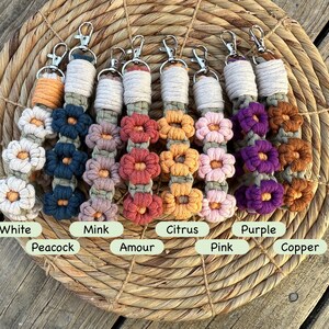 May include: Eight colorful macrame keychains with flower designs. The colors are white, peacock blue, mink, amour, citrus, pink, purple, and copper.