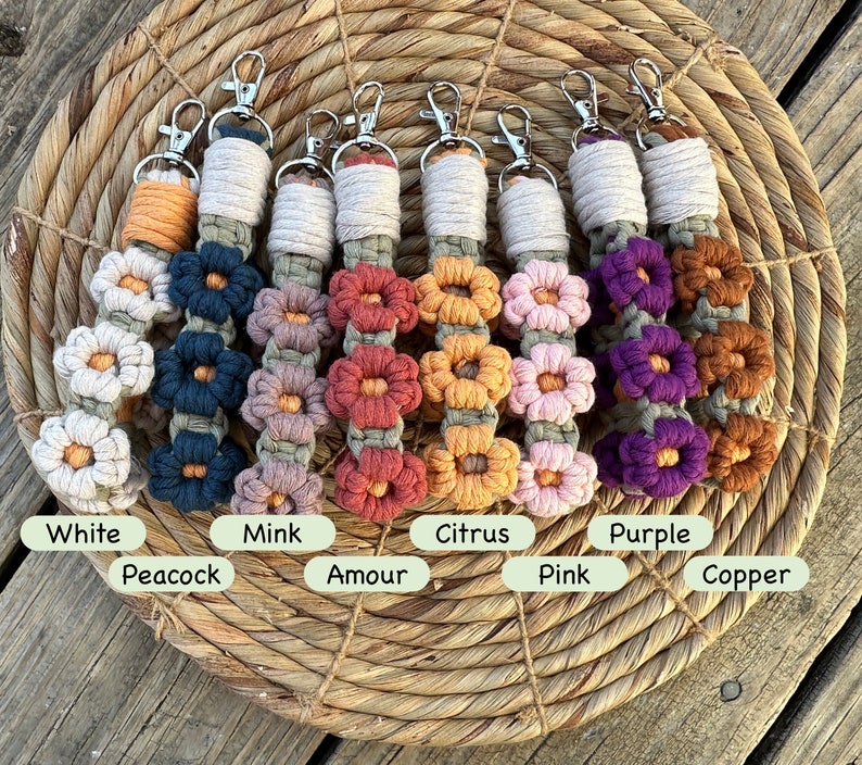 May include: Eight colorful macrame keychains with flower designs. The colors are white, peacock blue, mink, amour, citrus, pink, purple, and copper.