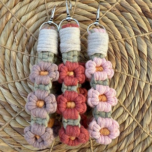 May include: Three crocheted keychains with floral designs. Each keychain features a series of pink, red, and green flowers with a light brown cord.