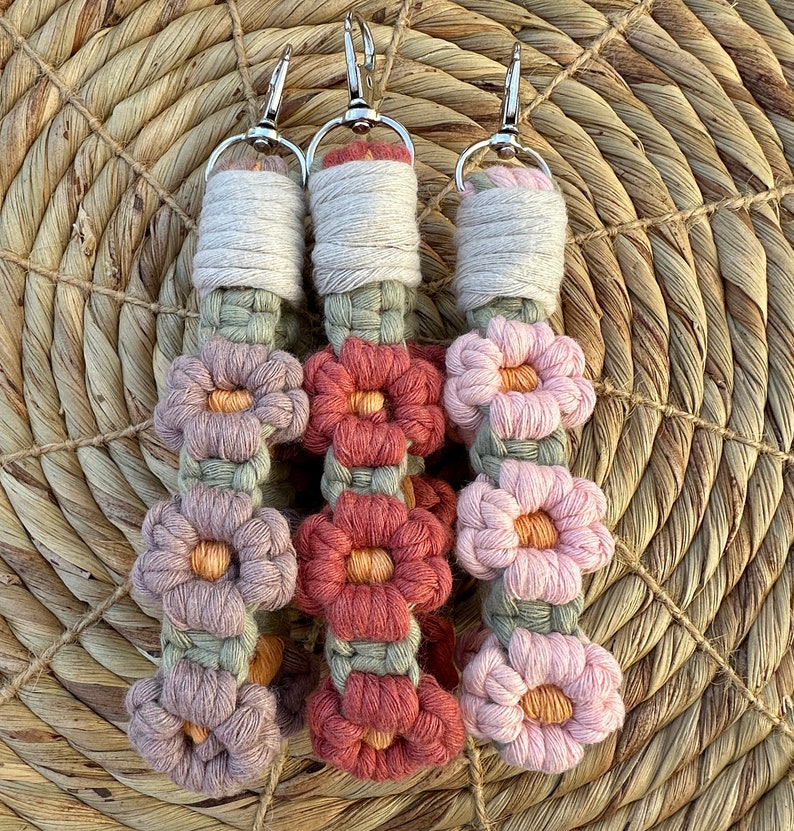 May include: Three crocheted keychains with floral designs. Each keychain features a series of pink, red, and green flowers with a light brown cord.