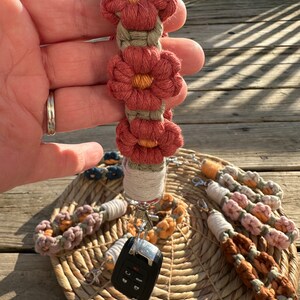 May include: A set of six colorful crocheted keychains with flower designs. The keychains are attached to a silver key ring and a black car key. The keychains are displayed on a woven basket.