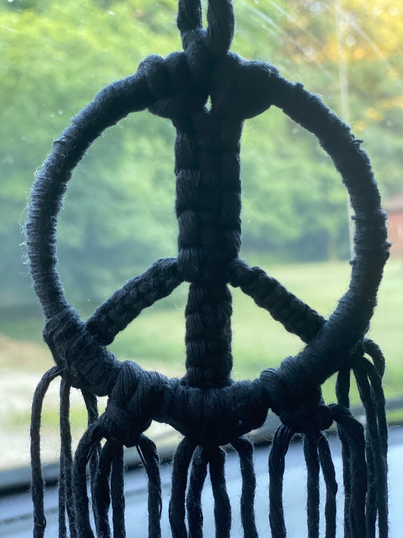 Peut inclure: Un symbole de paix en macram&eacute; noir avec de longues franges qui pendent du bas.