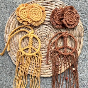 May include: Two macrame peace sign wall hangings with fringe and beads. One is brown and the other is yellow.