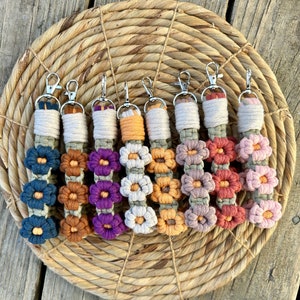 May include: Seven colorful crocheted flower keychains with silver key rings. The keychains are made with different colored yarn and feature a series of crocheted flowers.