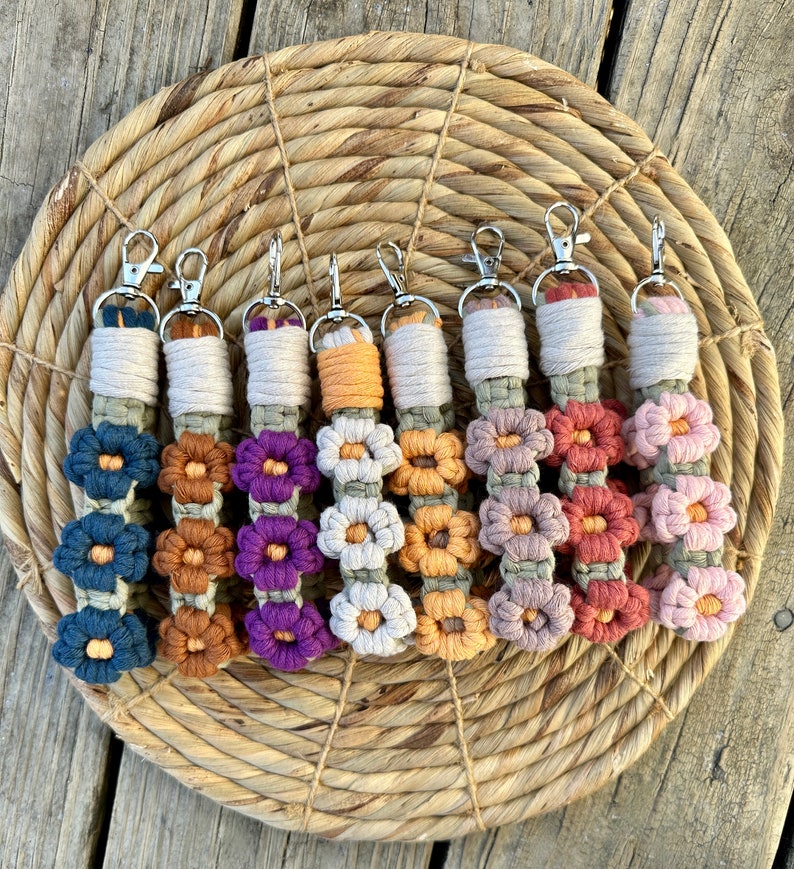May include: Seven colorful crocheted flower keychains with silver key rings. The keychains are made with different colored yarn and feature a series of crocheted flowers.