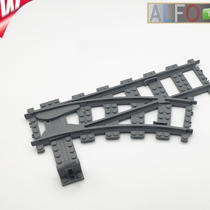 Op de afbeelding: Grijs plastic speelgoedtreinspoorstuk met een gebogen gedeelte en een wissel. Het spoor is ontworpen om aan te sluiten op andere treinspoorstukken.