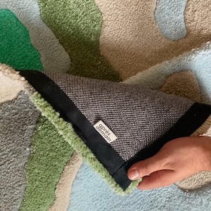 K&ouml;nnte beinhalten: Nahaufnahme der R&uuml;ckseite eines Teppichs mit einem schwarz-wei&szlig;en Muster. Der Teppich besteht aus einem weichen, pl&uuml;schigen Material und hat verschiedene Farben, darunter Gr&uuml;n, Blau und Beige. Der Teppich hat ein Etikett mit der Aufschrift "apr&egrave;s demain".