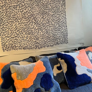 Op de afbeelding: Vier decoratieve kussens met een abstract patroon in blauw, oranje en grijs. De kussens zijn gemaakt van een zachte, pluche stof en hebben een reli&euml;fstructuur.
